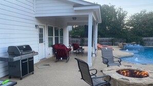A covered patio with a grill, outdoor furniture, and a stone fire pit.