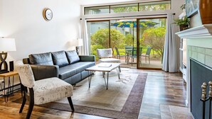 Un salon moderne avec un canapé en cuir, une table basse et un fauteuil. Une grande fenêtre offre une vue sur la verdure à l’extérieur.
