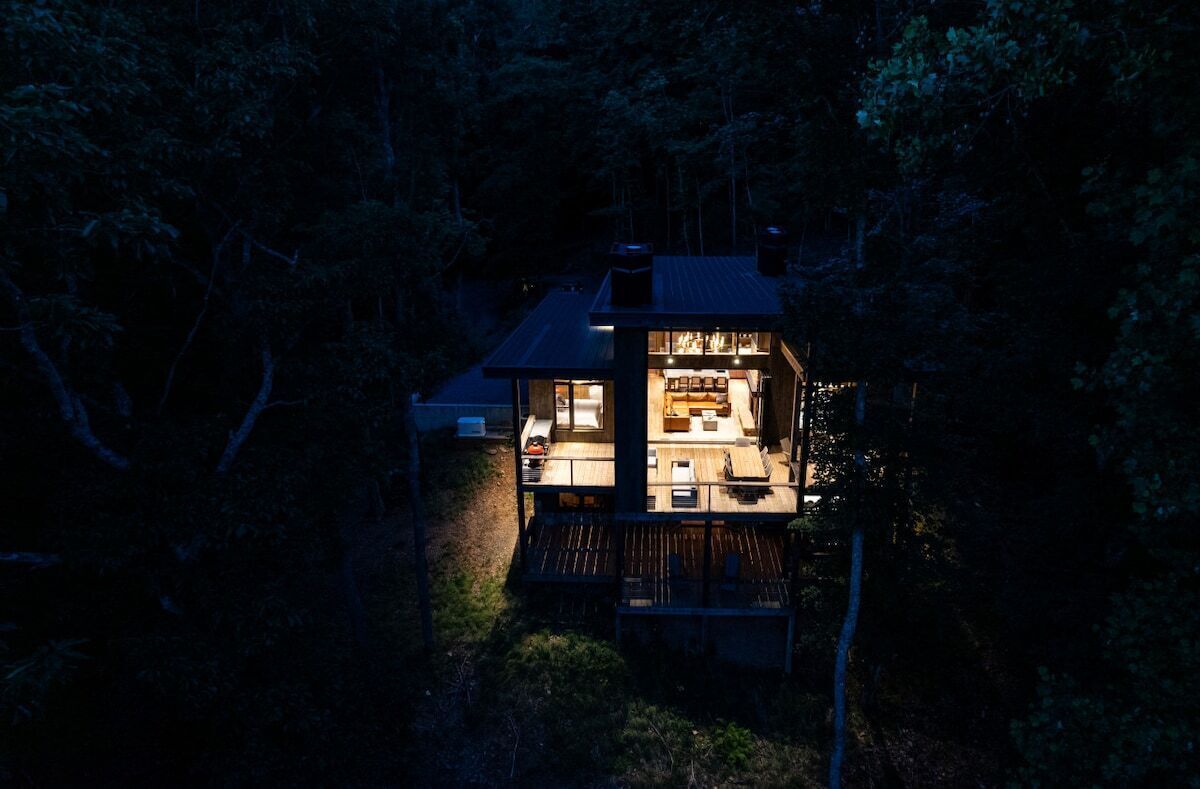 A two-story wooden cabin with a deck, surrounded by trees.