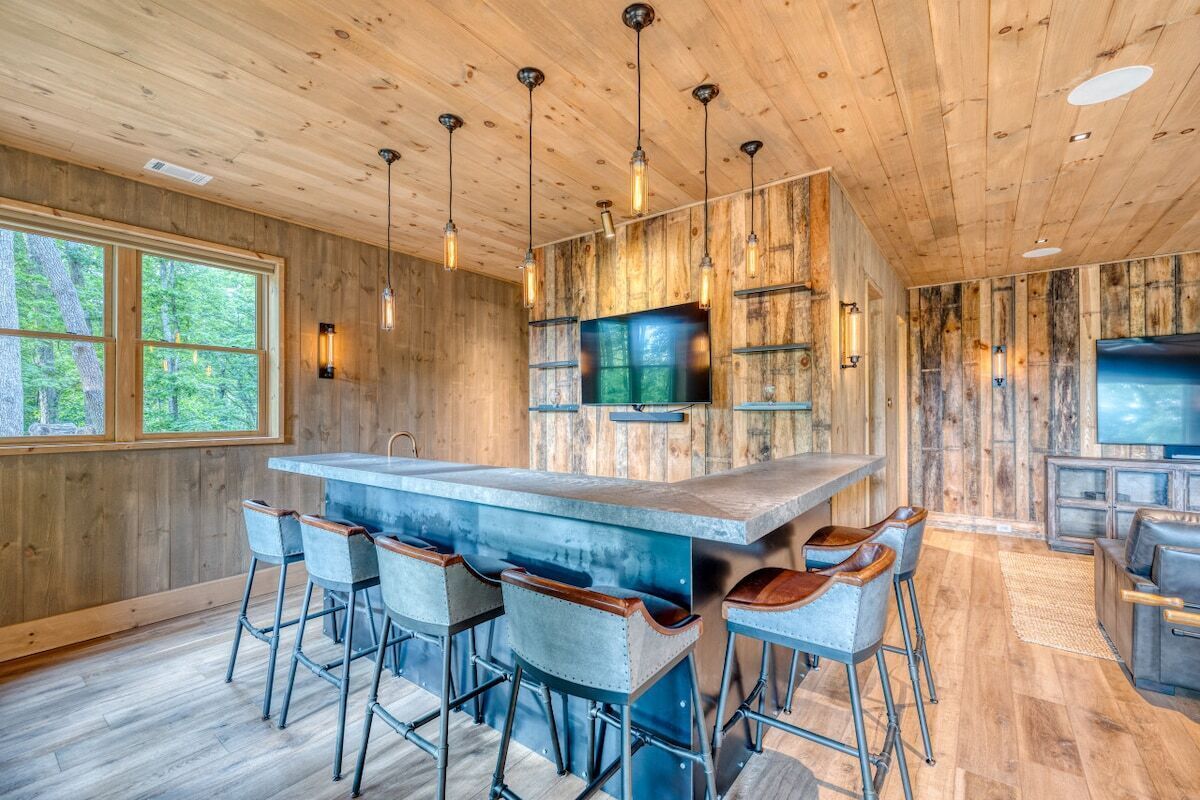 A wooden interior with a central island bar, bar stools, and a television.