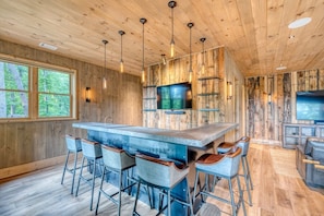 A wooden interior with a central island bar, bar stools, and a television.