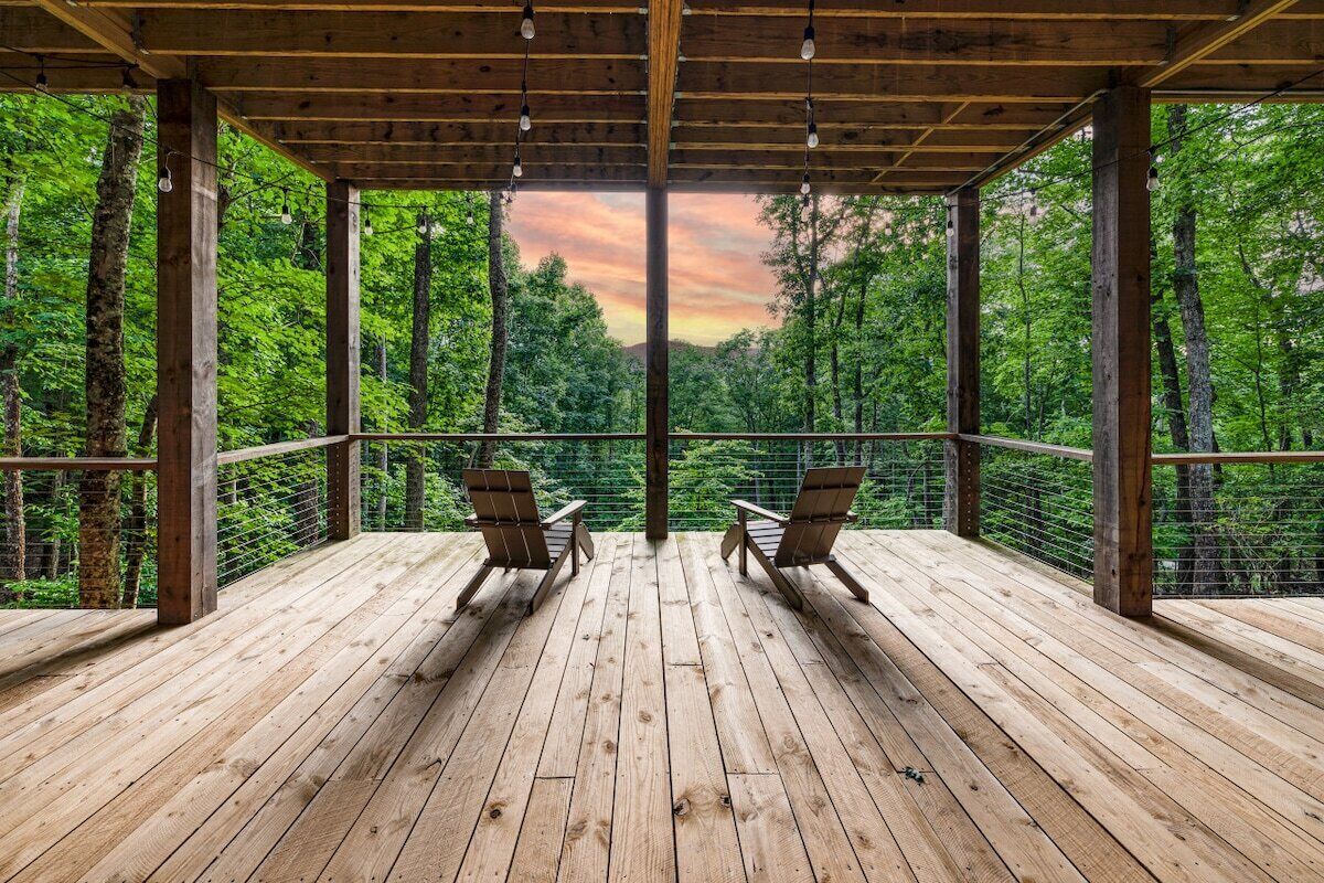 A wooden deck with two chairs facing a forested landscape.