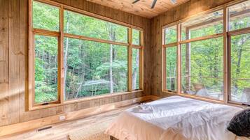 A bedroom with large windows, wooden walls, and a bed.