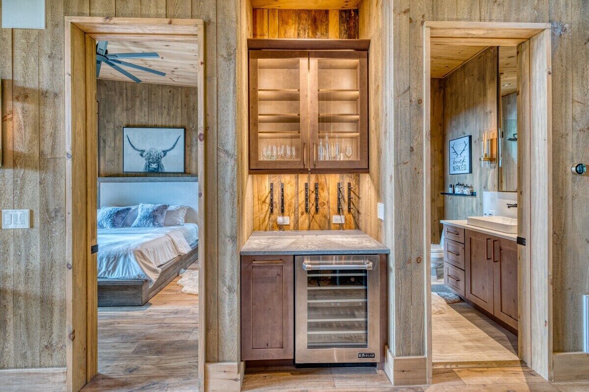 A modern interior with a central kitchen area, a bedroom with a bed and artwork, and a bathroom with a mirror and sink.