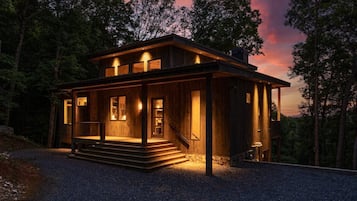 A wooden cabin with a porch, steps leading to the entrance, and a view of the surrounding forest.