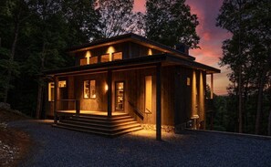 A wooden cabin with a porch, steps leading to the entrance, and a view of the surrounding forest.