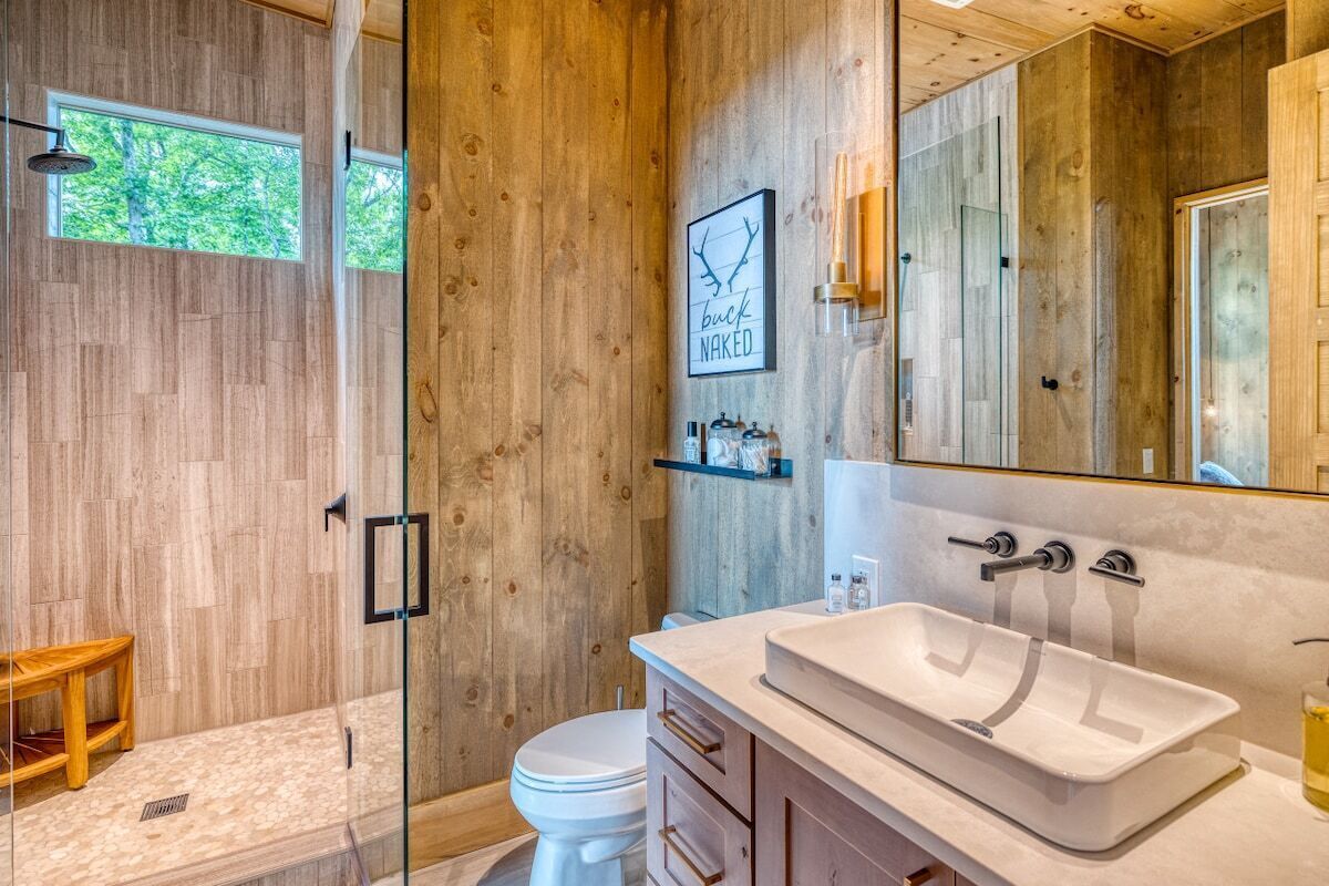 A bathroom with a wooden wall, a glass shower enclosure, a white sink, and a large mirror.