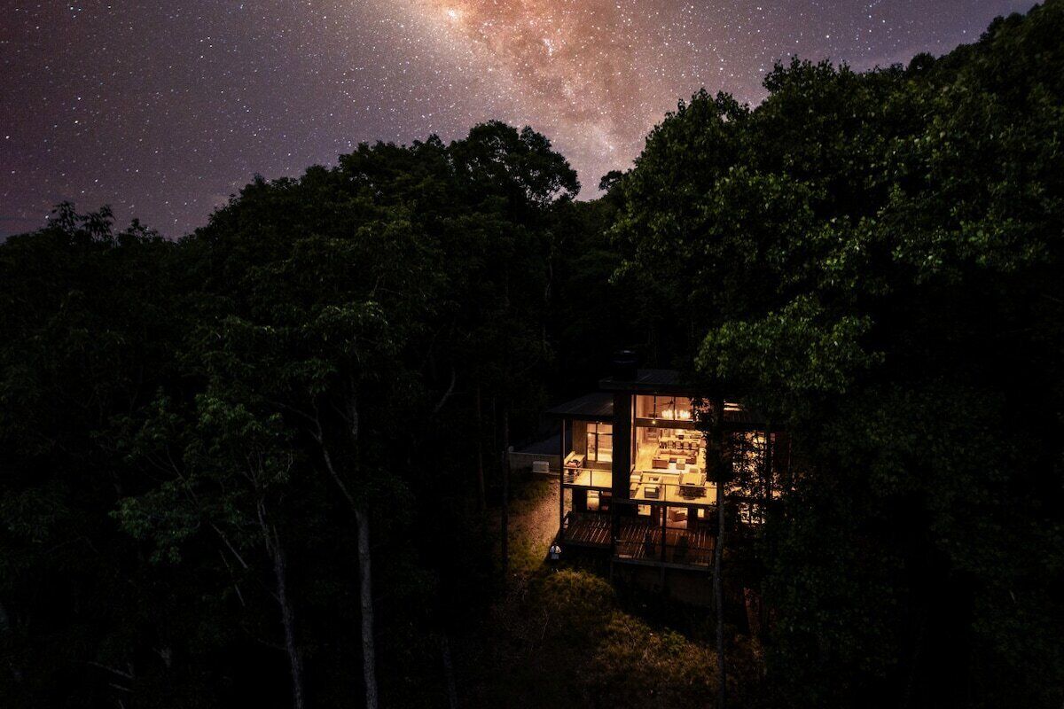 A cabin surrounded by trees with a view of the night sky.