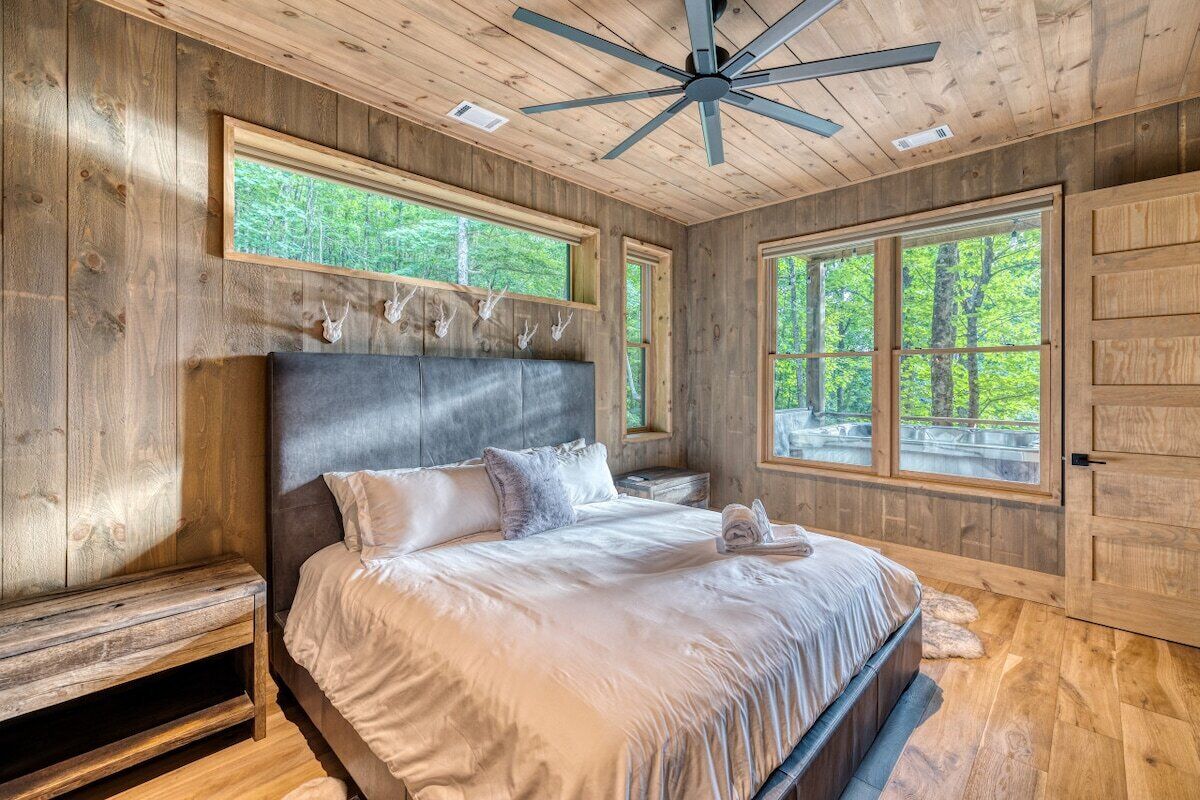 A bedroom with a large bed, wooden walls, and a ceiling fan.