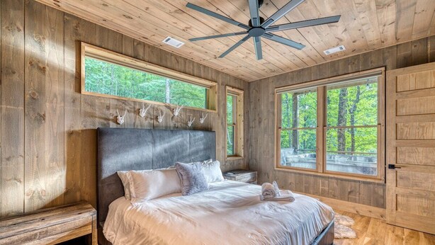 A bedroom with a large bed, wooden walls, and a ceiling fan. - Greenridge - Hot tub & mountain views (Blue Ridge Mountains)