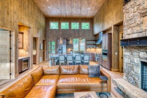 A spacious living area with a leather sofa, a stone fireplace, and a kitchen in the background.