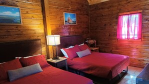A wooden cabin room with two beds, a nightstand with a lamp, a moose statue, and a window with pink curtains. - #29 - Flagpole View Cabins - Deluxe Cabin (Columbia Falls)
