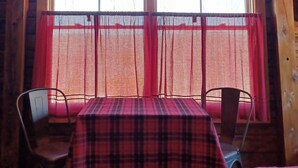 A rustic cabin interior with a wooden interior, a window with a deer silhouette, a plaid tablecloth, and two chairs. - #29 - Flagpole View Cabins - Deluxe Cabin (Columbia Falls)
