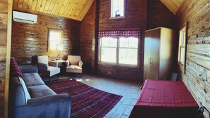 A cozy cabin interior with a wooden interior, a sofa, two armchairs, a table, and a window with a view. - #29 - Flagpole View Cabins - Deluxe Cabin (Columbia Falls)