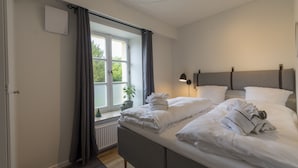 A neatly made bed with white linens and towels, a bedside lamp, and a window with curtains. - Guesthouse (Sønderborg)