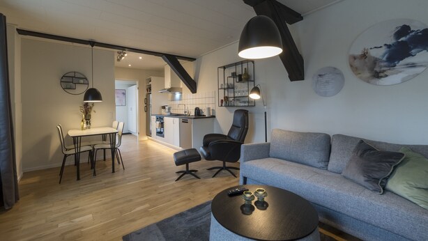 A modern living room with a grey sofa, a round coffee table, and a dining area with a table and chairs. - Guesthouse (Sønderborg)