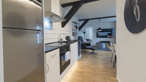 A modern kitchen with a built-in refrigerator, a stove, and a sink. There is a dining area with a table and chairs, and a television mounted on the wall. - Guesthouse (Sønderborg)