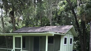 Eine kleine, eingeschossige Holzhütte mit Veranda und überdachter Eingangszone, umgeben von dichtem Wald.