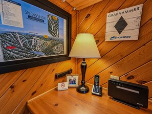 Pared de madera con un mapa enmarcado de Snowshoe Mountain, una lámpara, un teléfono, un router WiFi y un cartel de 'No Fumar'.