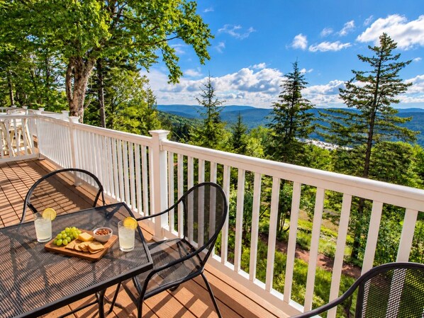 A deck with a table set for two, featuring a board with grapes, crackers, and a bowl of nuts, and two glasses of a clear beverage.