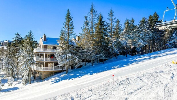 A multi-story building with balconies, surrounded by snow-covered trees and a ski slope.