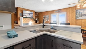 A modern kitchen with wooden paneling, a large window, and a view of a snowy landscape.