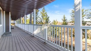 A covered wooden deck with white railings, leading to a building with a dark roof.