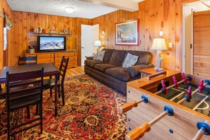 A cozy living room with a wooden interior, a television, a sofa, a coffee table, and a foosball table.