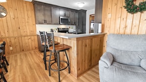 A kitchen with wooden cabinets, a microwave, and a bar area with stools.