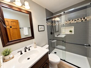 Un baño moderno con un espejo grande, un lavamanos blanco, un inodoro y una zona de ducha con paredes de vidrio.