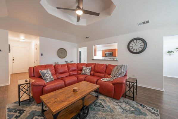 A modern living room with a red leather sectional sofa, a wooden coffee table, and a patterned rug.