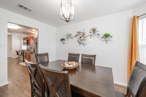 A dining area with a wooden table and chairs, a chandelier, and wall-mounted shelves with plants.