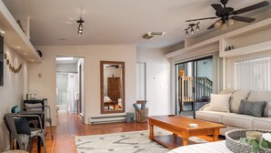 A spacious living area with a sofa, coffee table, and a dining table with chairs. There is a large mirror, a ceiling fan, and a staircase leading to an upper level. - Gorgeous Gem in West Sedona (Sedona)
