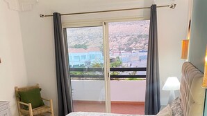 Un dormitorio con cama, una silla, una mesita de noche, una lámpara y vistas al exterior.