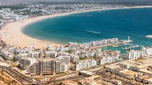 Un paisaje urbano costero con playa, puerto deportivo y edificios residenciales densos.