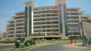 Un edificio de varios pisos con balcones, un cartel de estacionamiento y una zona ajardinada en la parte frontal.