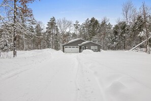 Una casa a due piani con un garage, immersa in un paesaggio innevato e alberato.