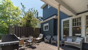Een overdekt terras met een barbecue, rieten meubilair en een comfortabele bank.