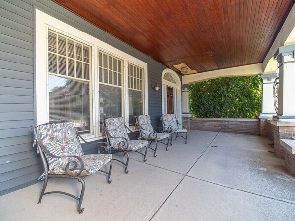 A covered patio with four chairs, a wooden ceiling, and a brick wall with greenery. - The Captain's Quarters (Dunkirk)