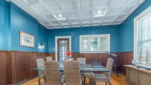 A dining room with a round table, wicker chairs, wooden paneled walls, and a ship model on a counter. - The Captain's Quarters (Dunkirk)