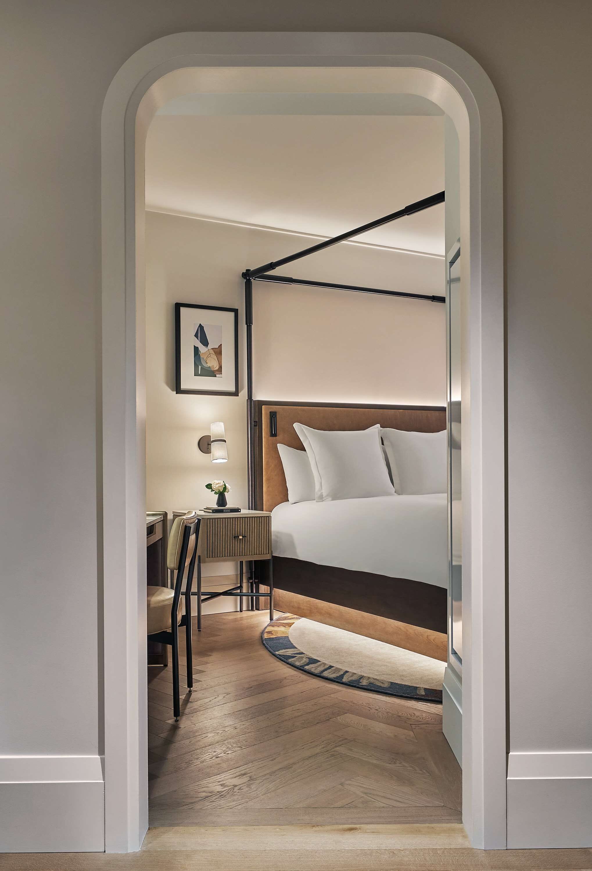 A hotel room with a bunk bed, a desk with a chair, a small table with a vase, and a framed picture on the wall.