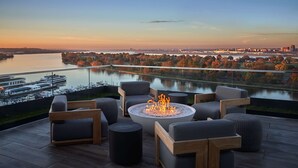 A deck with outdoor seating and a fire pit, overlooking a river and cityscape. - Pendry Washington DC - The Wharf (Washington)