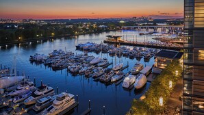 A marina with multiple boats docked, a bridge in the background, and a modern building on the right. - Pendry Washington DC - The Wharf (Washington)