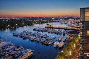 A marina with multiple boats docked, a bridge in the background, and a modern building on the right.
