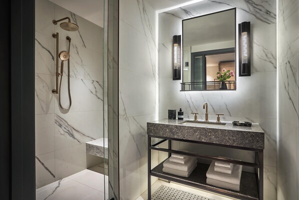 Une salle de bain moderne dotée d’une douche à parois de verre, d’un mur recouvert de carreaux de marbre, d’un grand miroir et d’une étagère intégrée où sont rangées les serviettes.