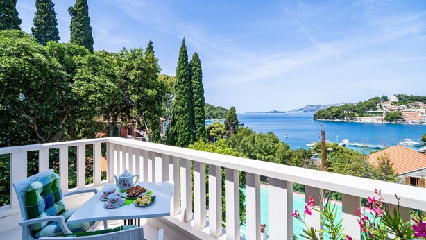 Un balcon avec une table préparée pour le thé, offrant une vue sur la côte, avec des bateaux et une île au loin.