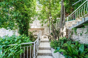 Steps lead up to a traditional staircase surrounded by lush greenery and climbing plants.