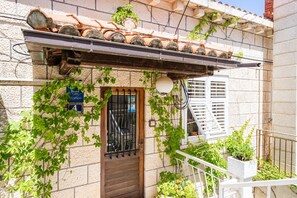Traditional building with a stone facade and tiled roof, featuring a wooden door and lush greenery.