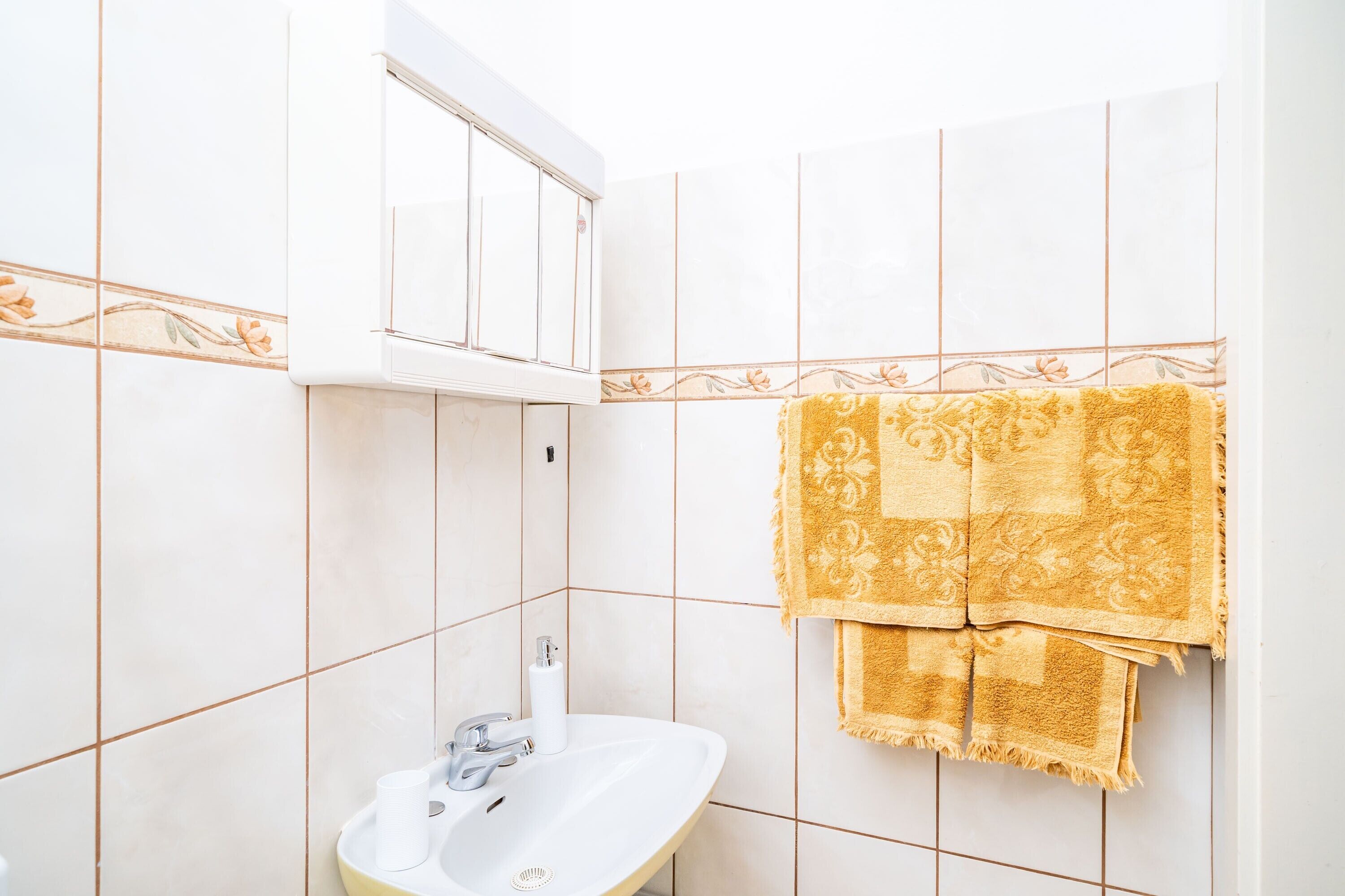A bathroom with a white sink, a mirror, and a towel rack with a yellow towel.