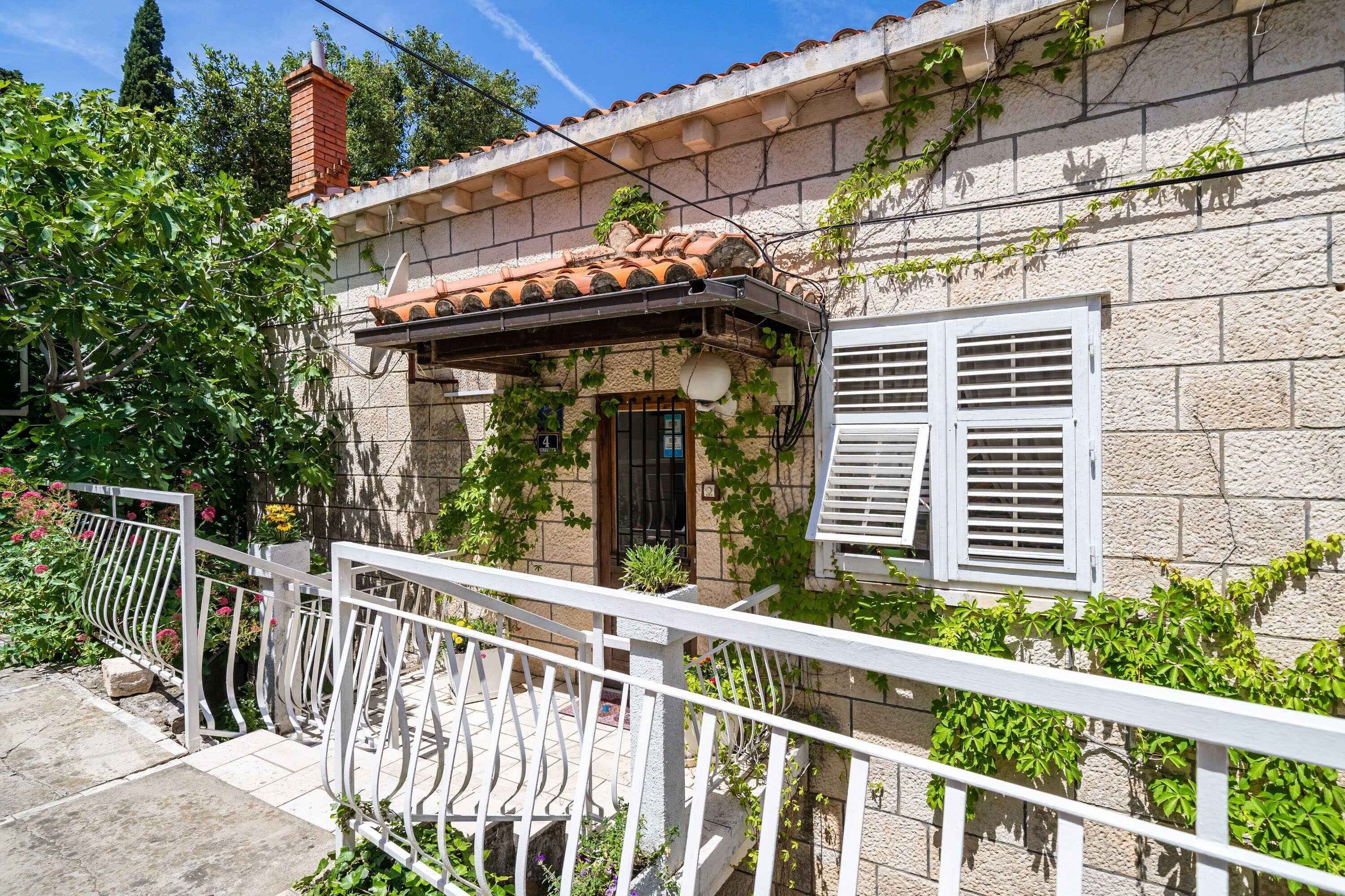 A stone house with a tiled roof, white shutters, and a white balcony railing.